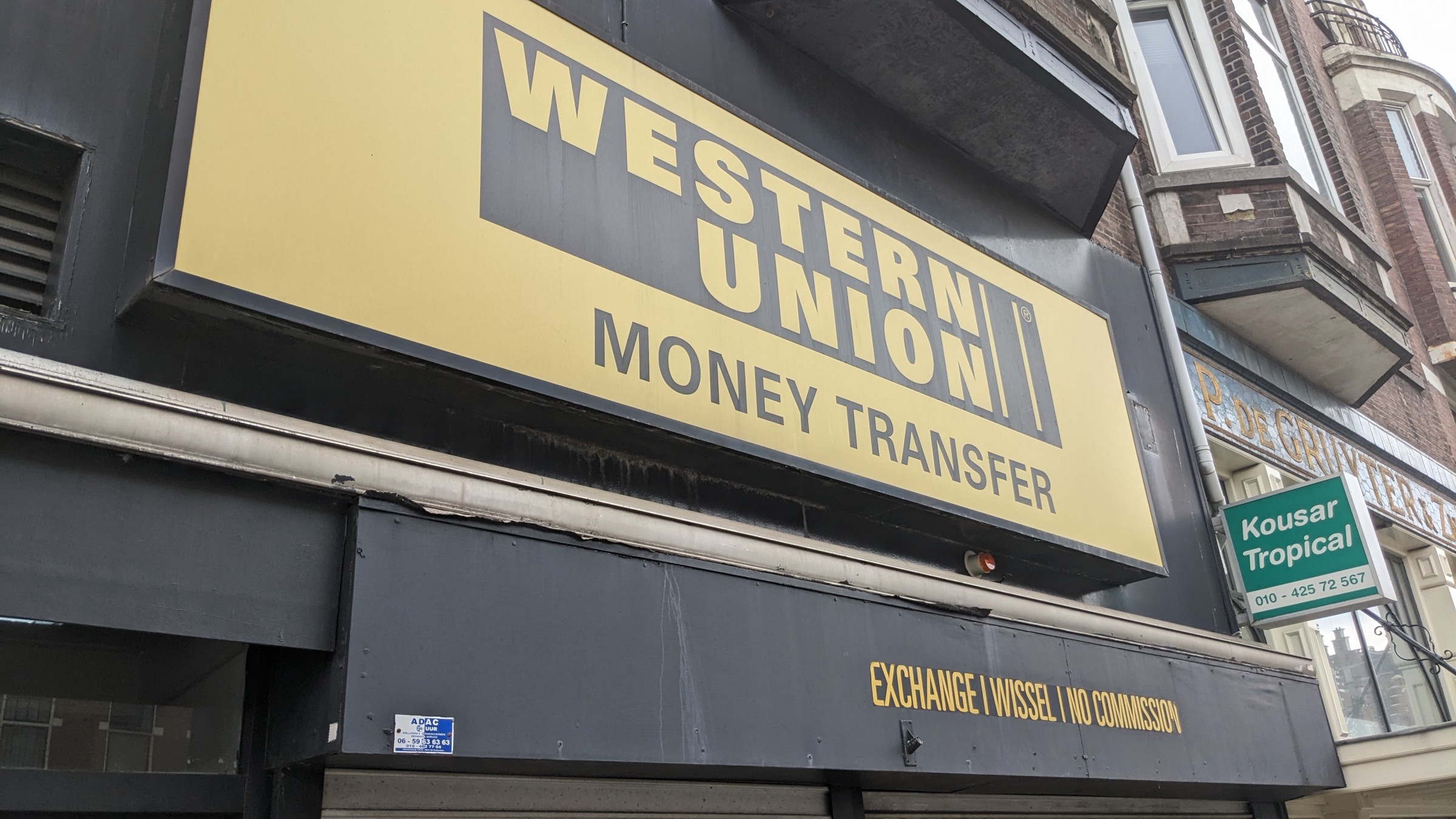 A large Western Union Money Transfer sign above a shopfront, with a fascia band reading exchange, wissel, no commission.