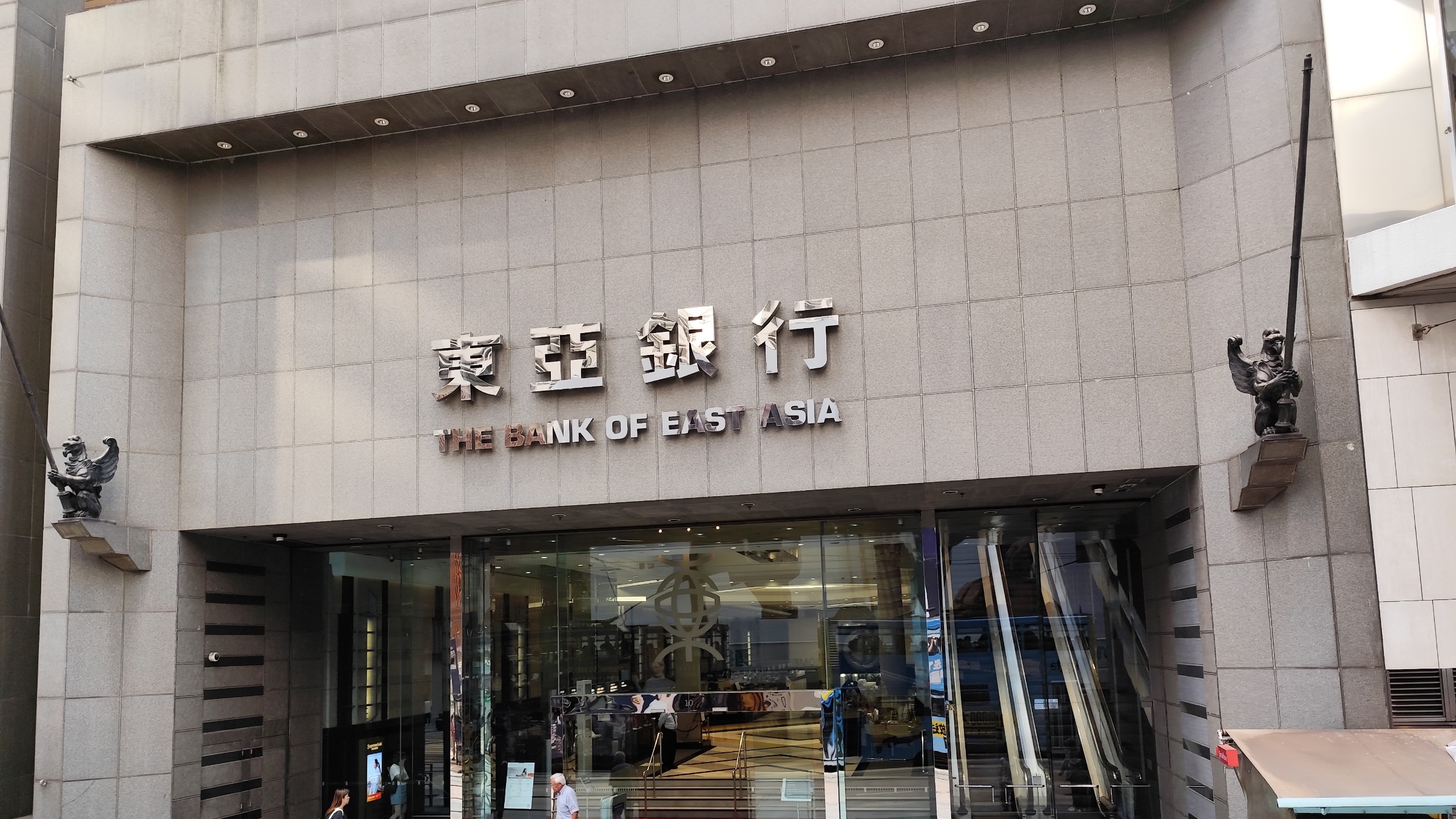 The entrance to The Bank of East Asia headquarters on Des Voeux Road Central, Hong Kong, with the bank's name in Chinese and English above the doors.