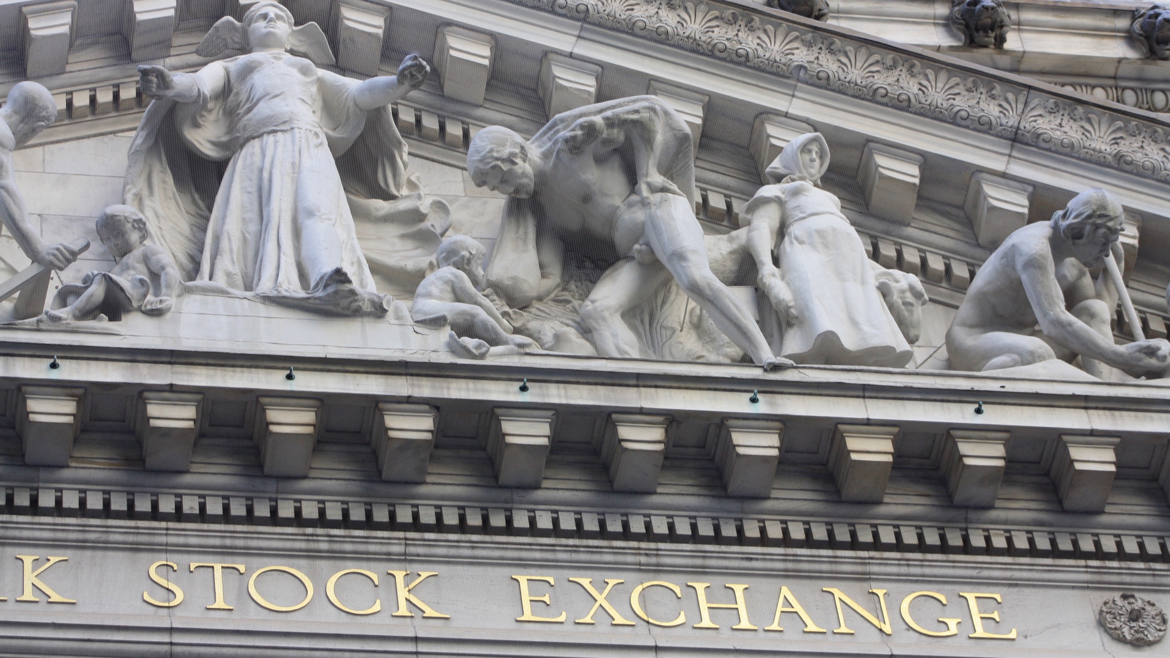 The carved pediment of the New York Stock Exchange building with the words STOCK EXCHANGE in gold lettering on the entablature below it.