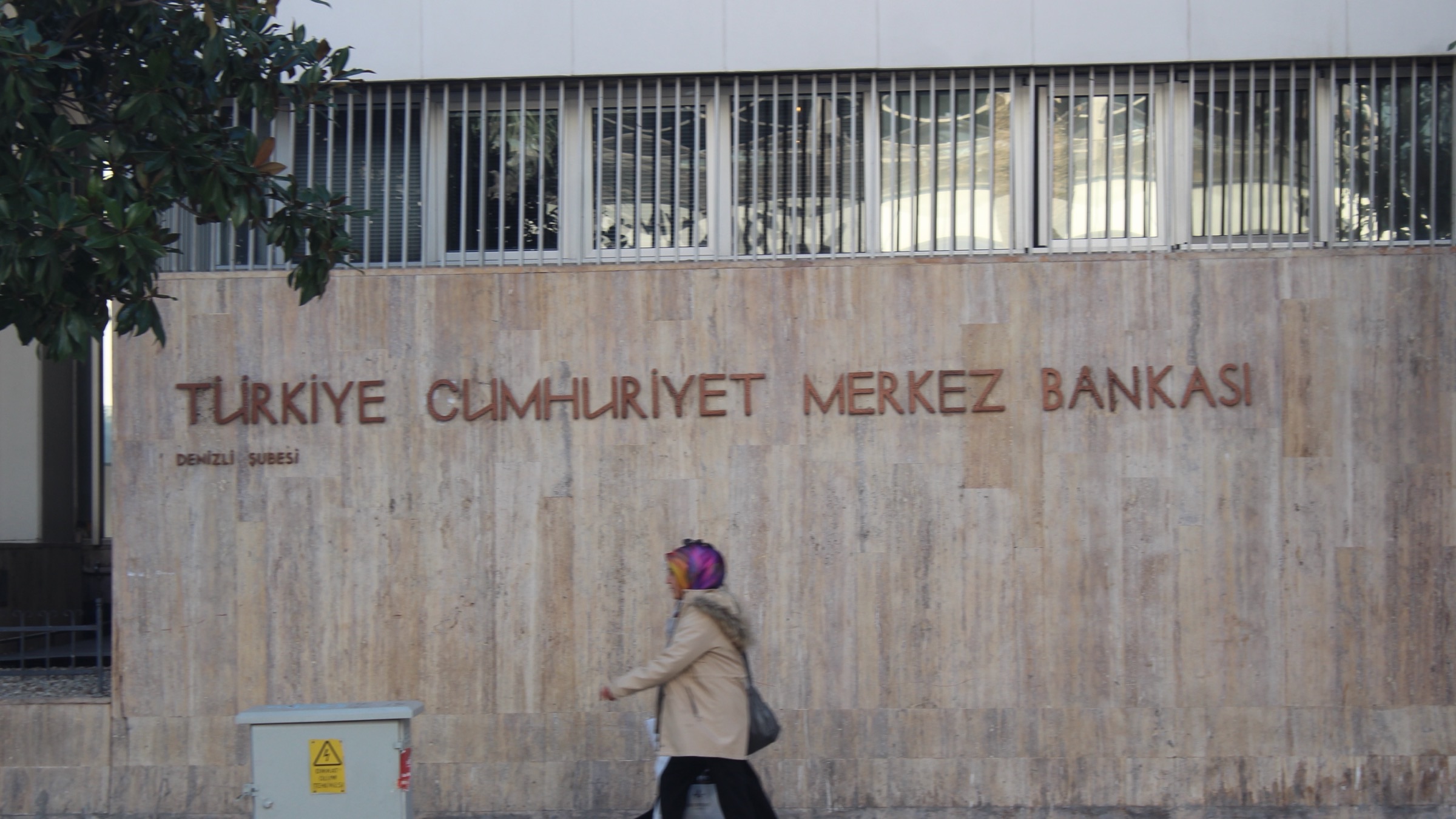 The words Türkiye Cumhuriyet Merkez Bankası cut into the stone facade of a Central Bank of the Republic of Turkey building, with a pedestrian walking past.
