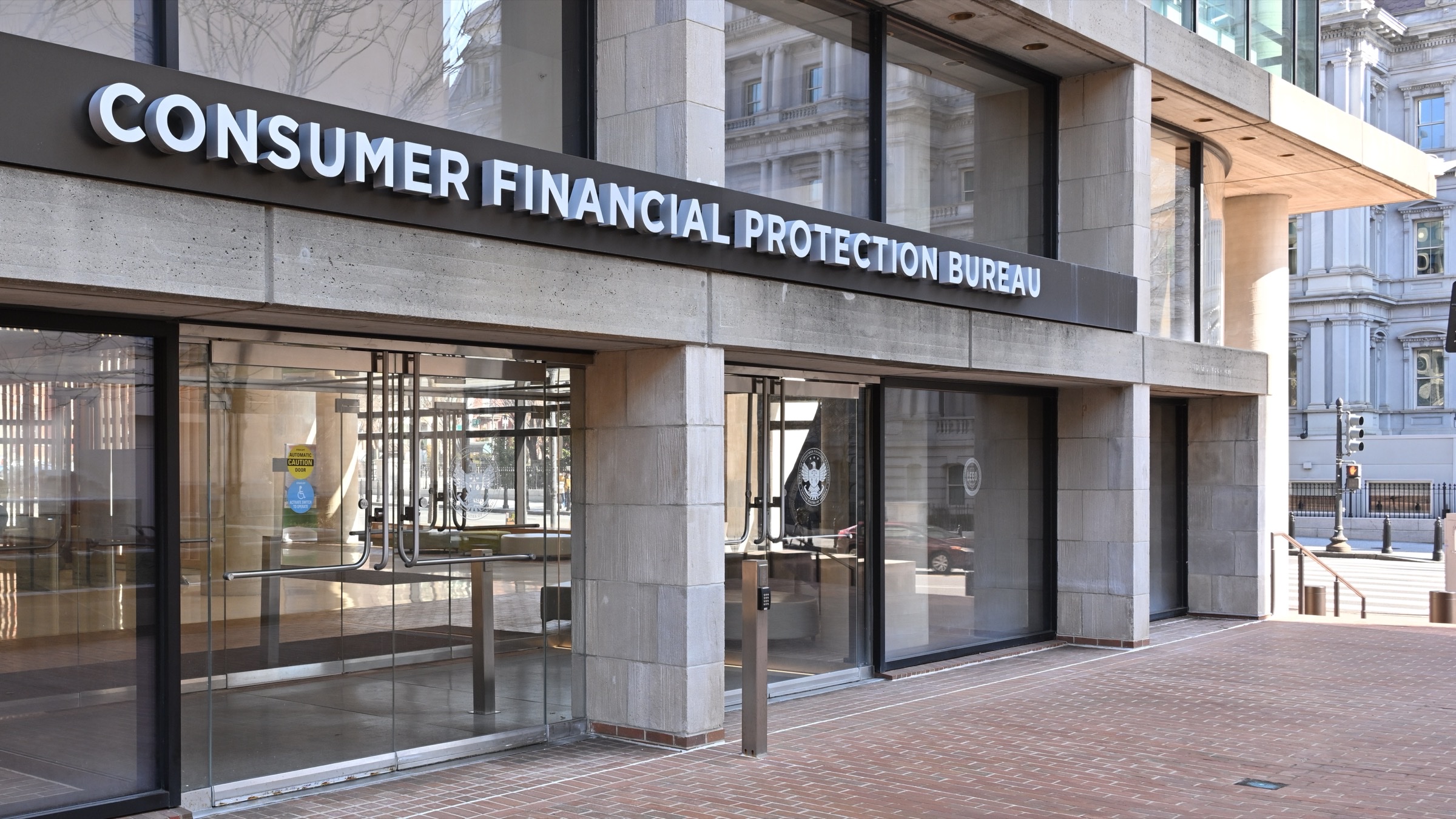 The entrance to the Consumer Financial Protection Bureau headquarters in Washington, with the bureau's name in large letters above the glass doors.