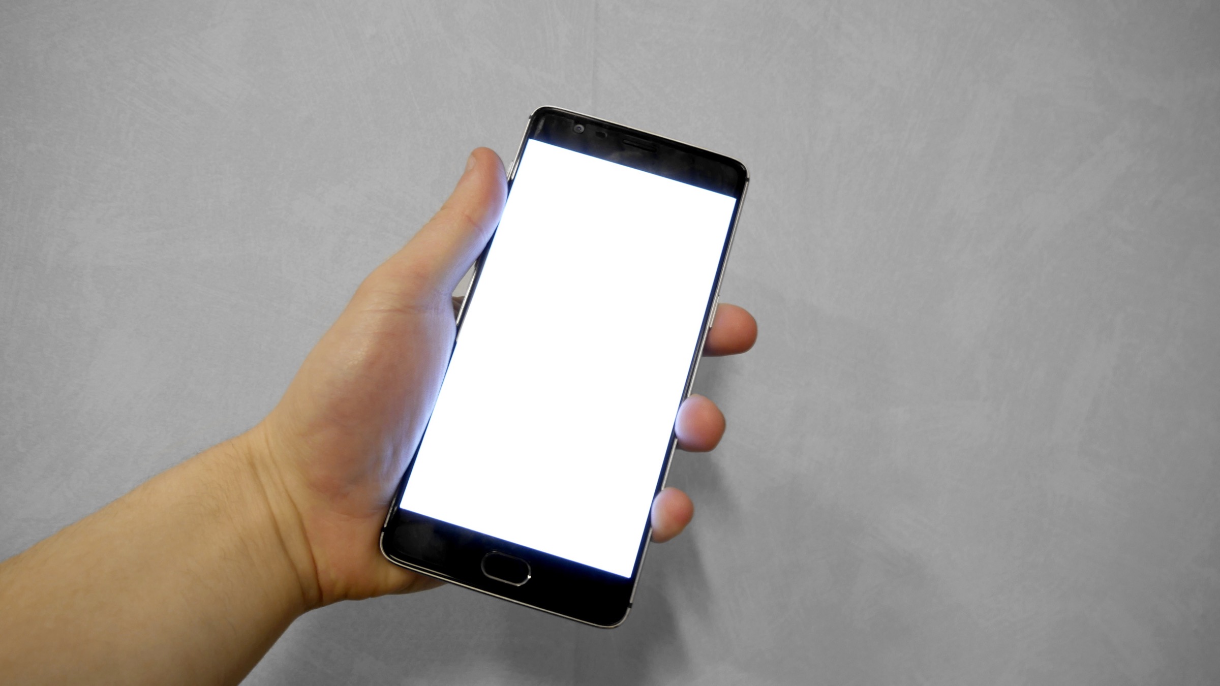 A hand holding a smartphone with a blank white screen against a plain grey background.