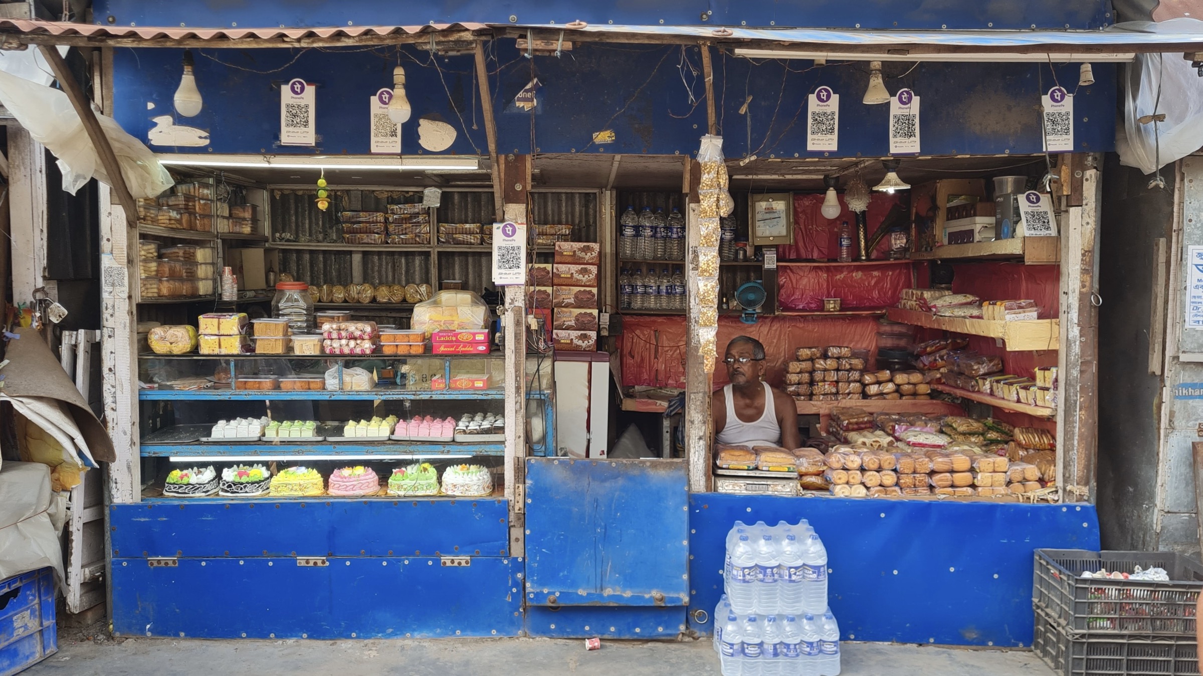 A sweet and bakery shop in West Bengal with six PhonePe and BHIM UPI QR code stickers displayed along the shopfront.