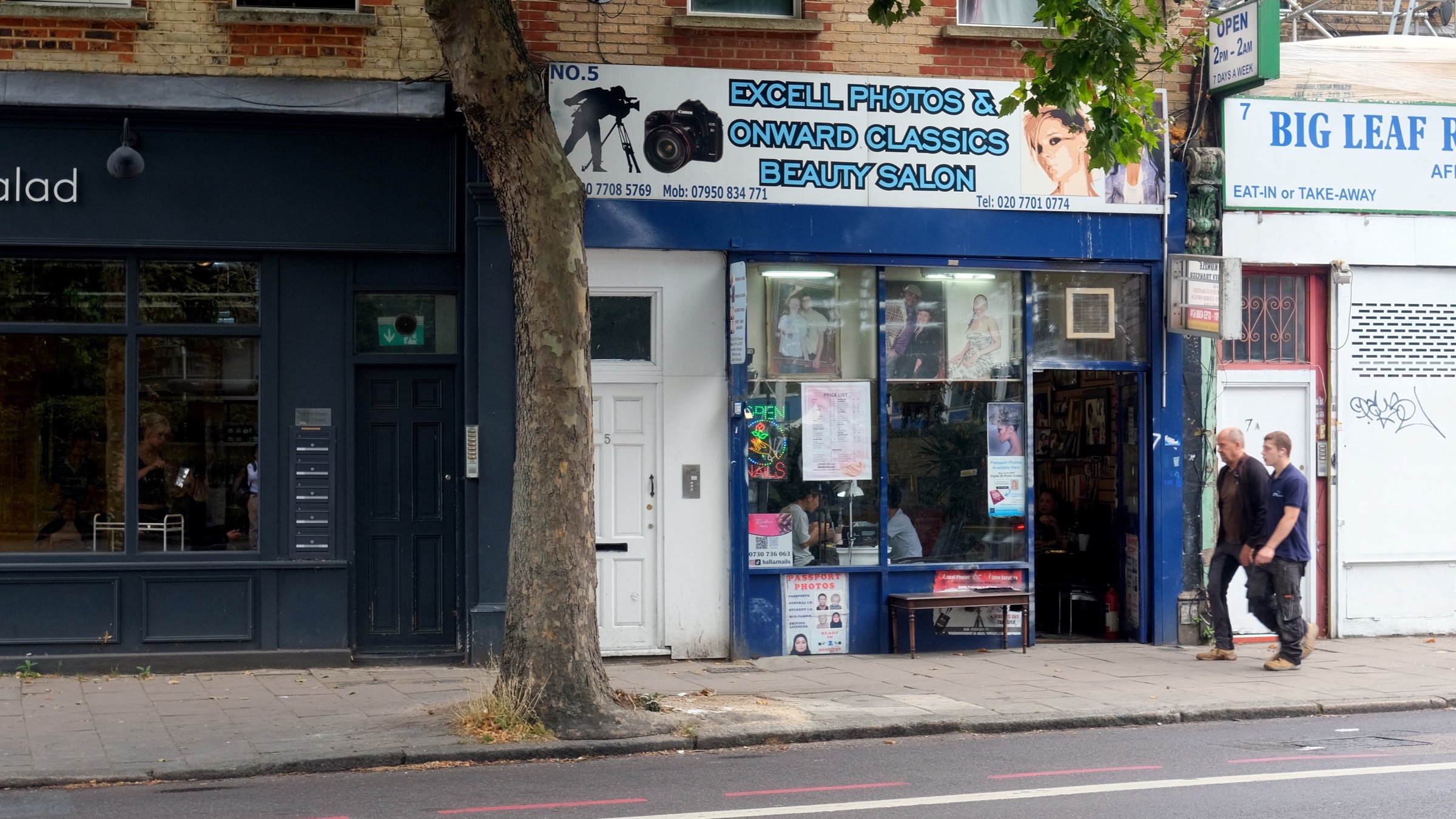 Shopfronts on Peckham High Street in south London, including an African takeaway, a photo shop and a beauty salon, with two people walking past.