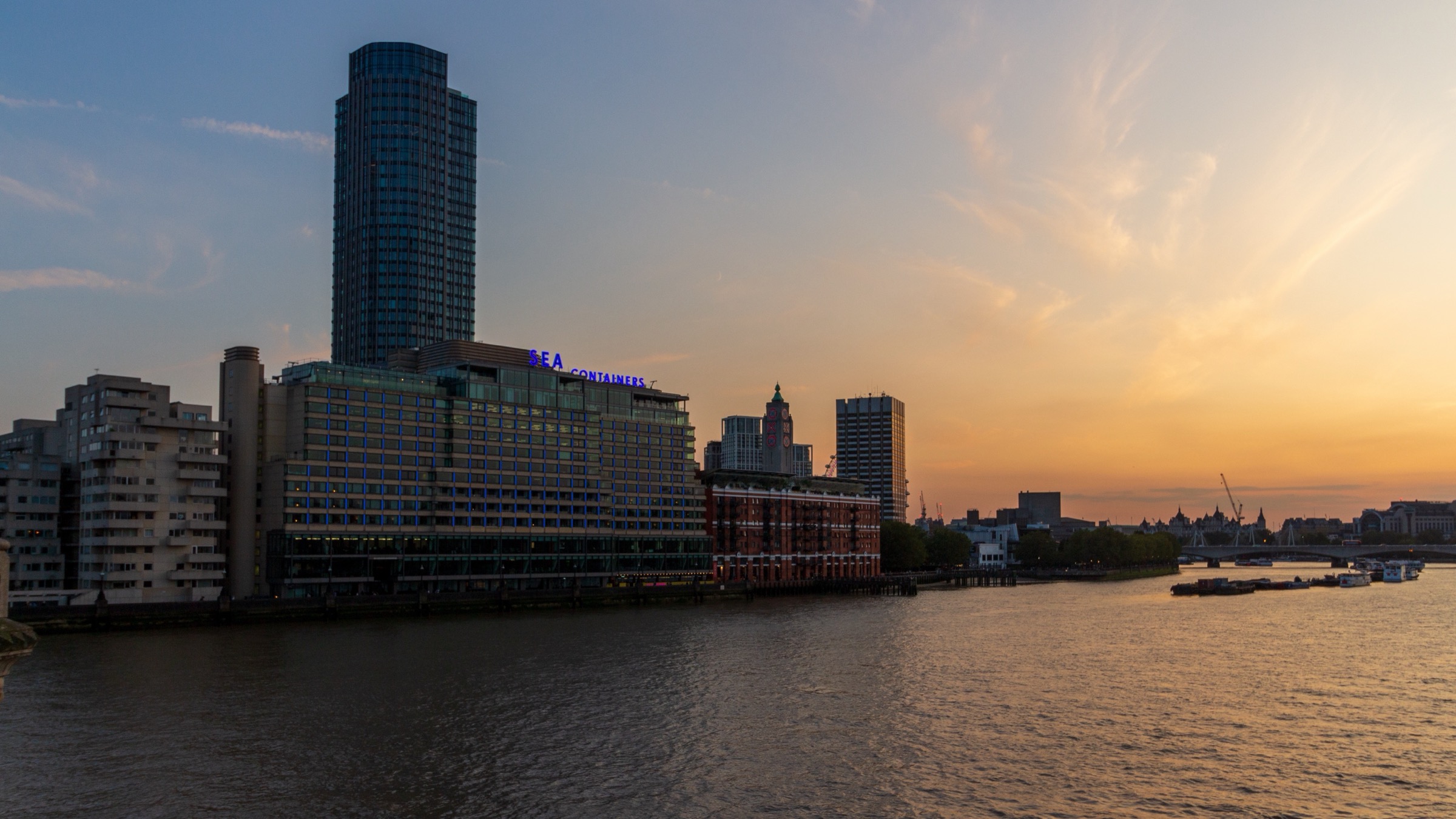 Sea Containers House on the south bank of the River Thames in London at dusk, with its illuminated rooftop sign and a tower behind it.