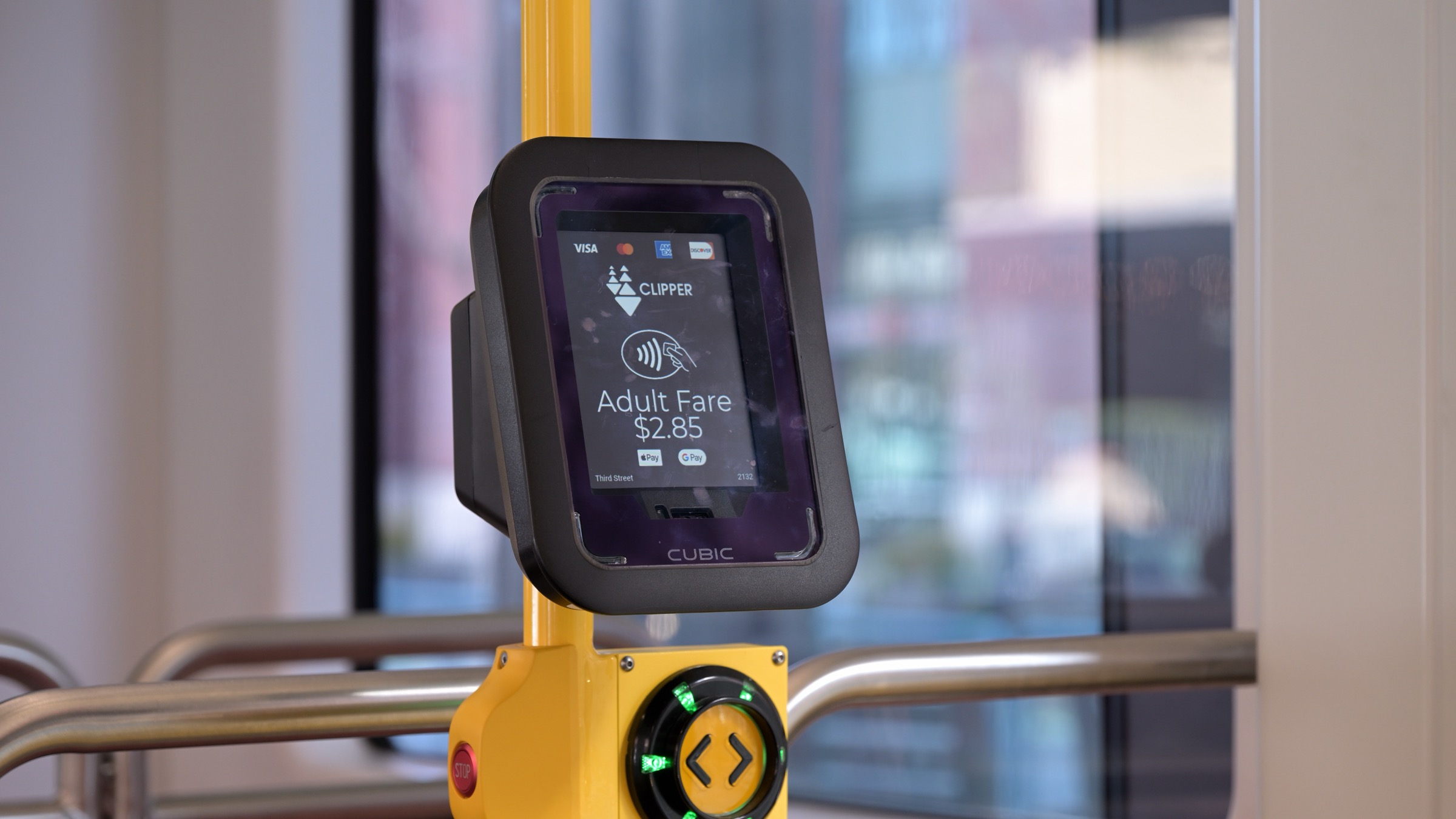 A contactless card fare reader on a San Francisco Muni tram, its screen showing a tap symbol and an adult fare of 2.85 dollars
