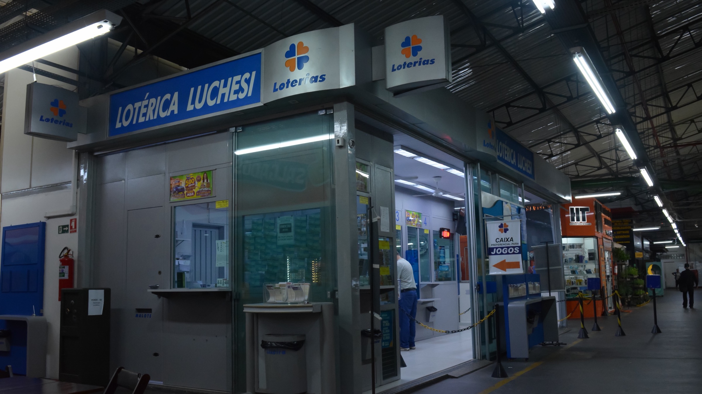 A lottery outlet under the Caixa Loterias brand inside a covered municipal market, with service counters and a sign reading Loterica Luchesi