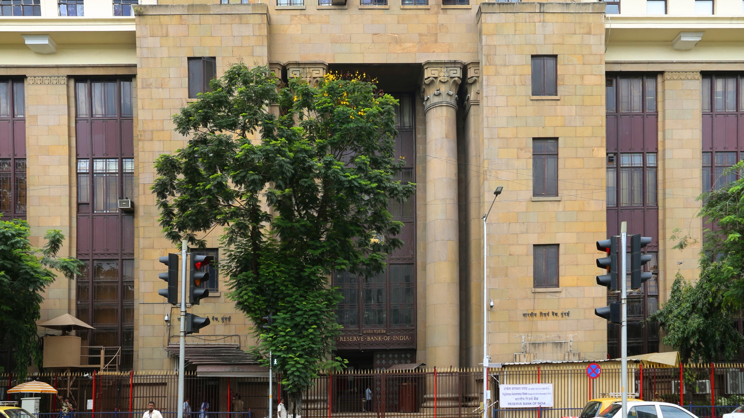 The stone facade and columned entrance of a Reserve Bank of India building in Mumbai, with the bank’s name above the door and traffic lights in front