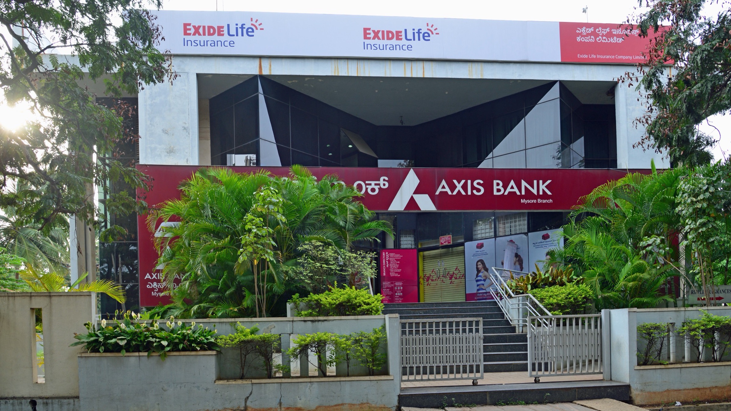 The front of an Axis Bank branch on Temple Road in Mysore, India, with the bank’s red signboard above the entrance steps and tropical plants in front