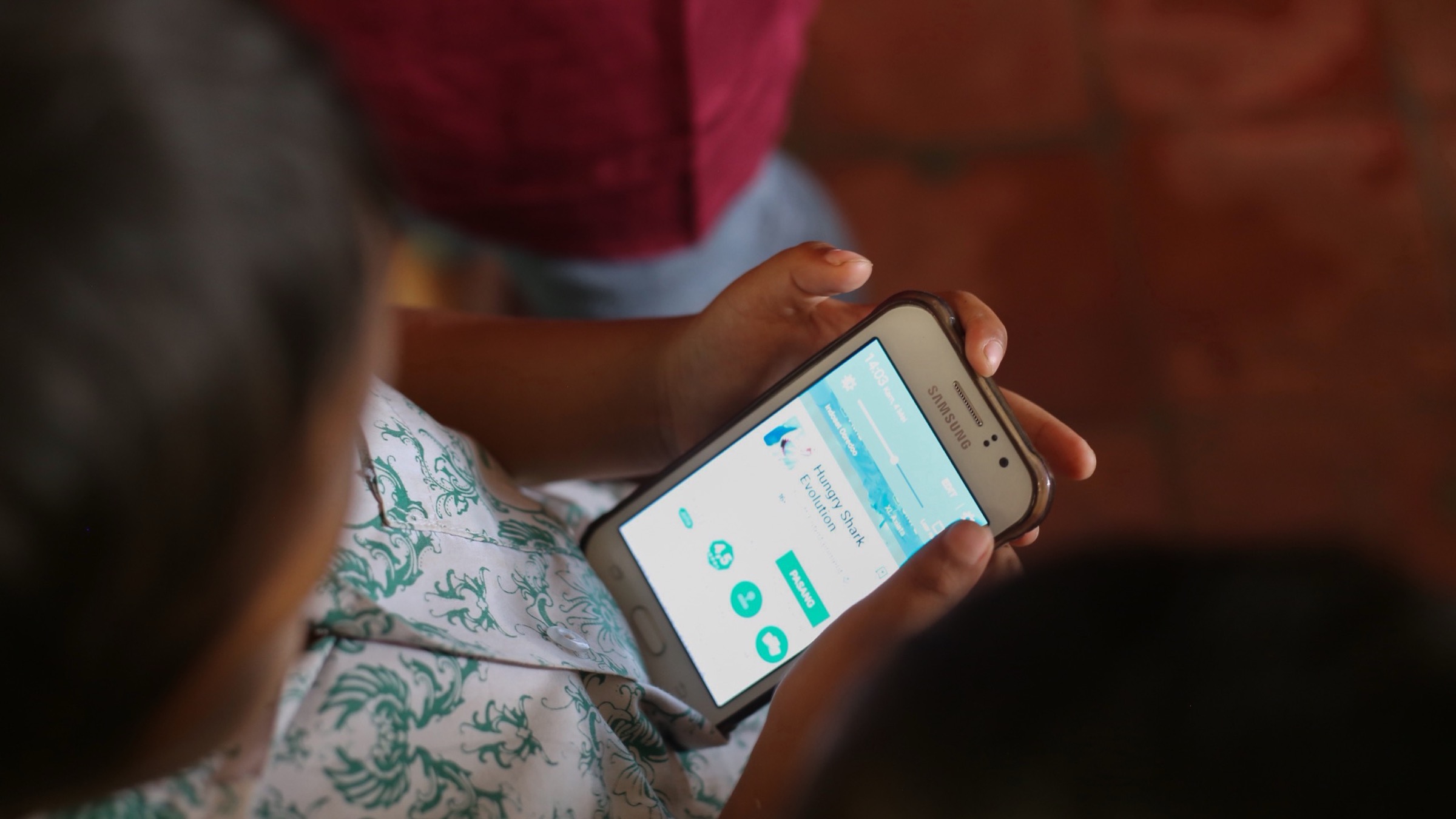 A child holds a Samsung Android phone showing a game’s install page in the Google Play Store, photographed from above in Bandung, Indonesia