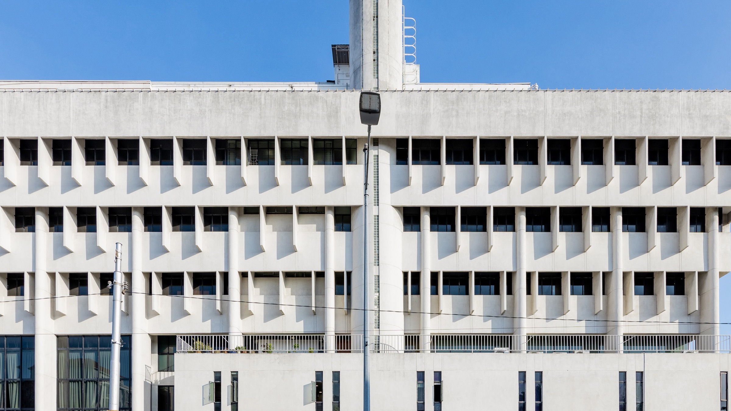 The white concrete facade of Bank Negara Malaysia’s Penang branch, with rows of deep-set windows under a clear blue sky